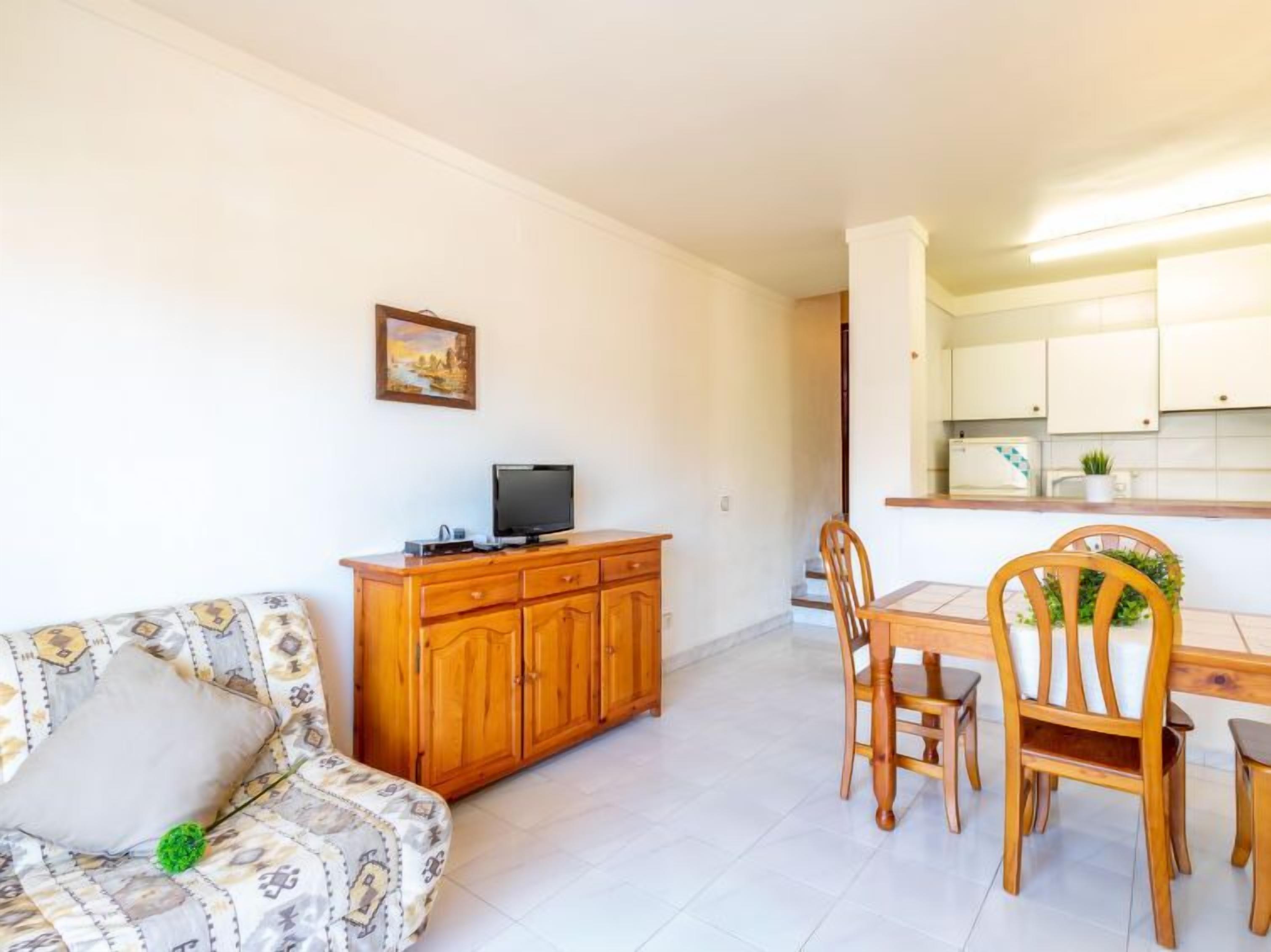 A living room with a sofa, a wooden cabinet, a television, and a dining area with chairs and a table.