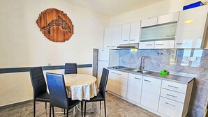 A compact kitchen with white cabinets, a marble backsplash, and a dining area with a round table and four chairs. - Snježana by Interhome (Korcula/Zavalatica)
