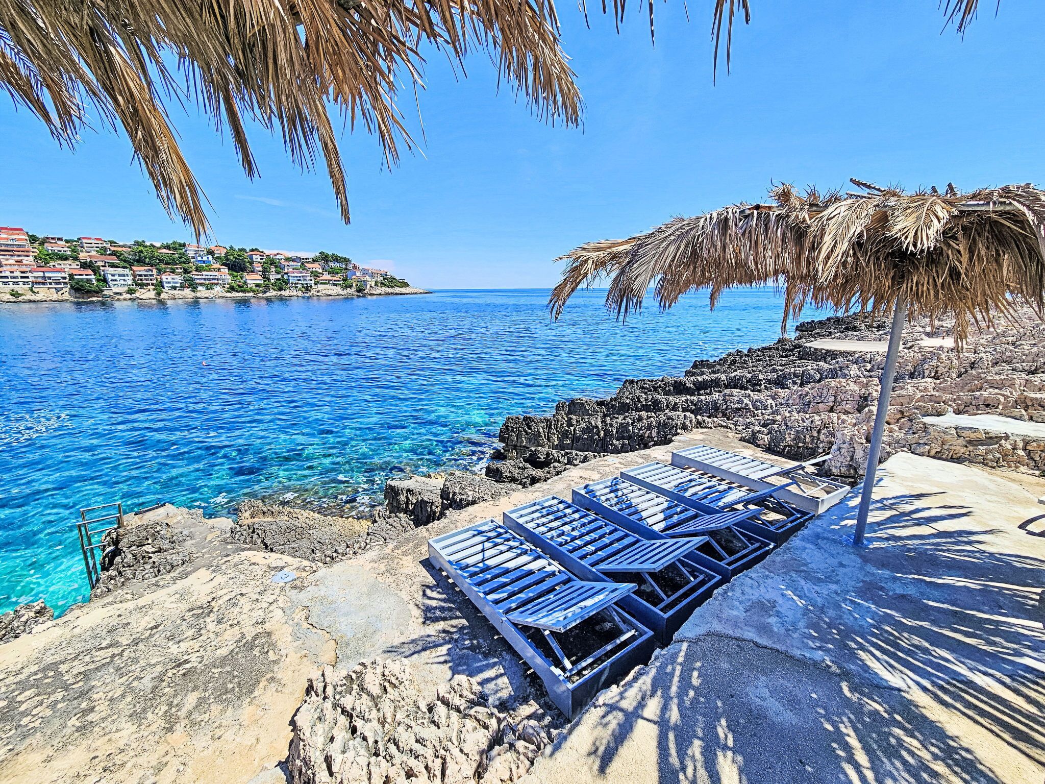 Una spiaggia con acqua cristallina, lettini e un ombrellone di paglia.