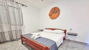 A bedroom with a wooden bed, a white wall, a wooden artwork, and a small bedside table. - Snježana by Interhome (Korcula/Zavalatica)