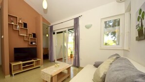Een woonkamer met een bank, een televisie, een houten tafel en een schuifpui naar een balkon.