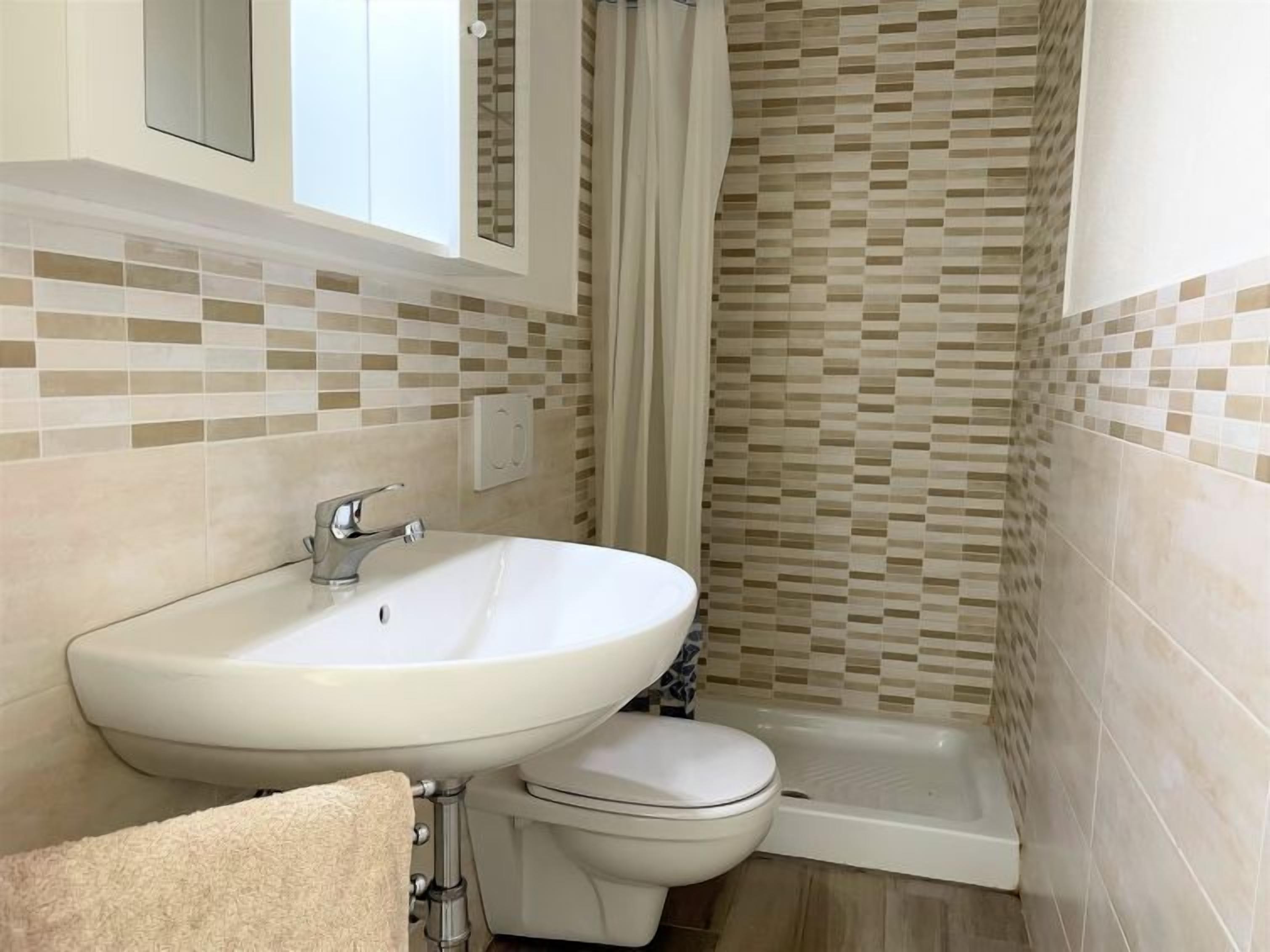 A bathroom with a white sink, toilet, and shower. The walls have a mosaic tile pattern.