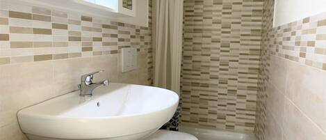 A bathroom with a white sink, toilet, and shower. The walls have a mosaic tile pattern.