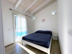 A bedroom with a bed, a window with curtains, a ceiling fan, and a light switch.