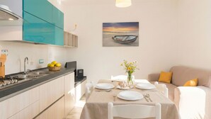 A modern kitchen with a dining area, a painting of a boat on water, and a sofa with cushions. - Bellina by Interhome (La Caletta)