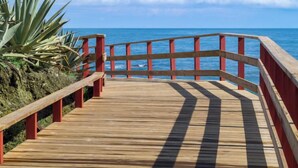 A wooden boardwalk with red railings leading to the ocean.