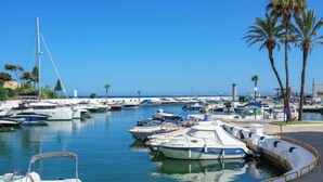 A marina with various boats docked, a clear blue sky, and palm trees.