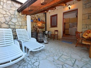 A stone-walled patio with white plastic chairs, wooden chairs, and a rustic wooden table.