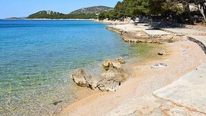 Une plage côtière aux eaux cristallines, bordée de rochers, avec une chaîne de montagnes en arrière-plan.