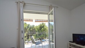 Une pièce dotée d’une porte-fenêtre coulissante donnant sur un balcon extérieur avec une table et des chaises.