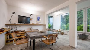 Un comedor moderno con una mesa grande, sillas, un televisor y vistas a zonas verdes a través de amplios ventanales.