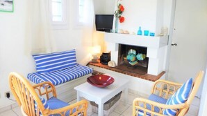 Ein gemütliches Wohnzimmer mit einer Couch, zwei Korbstühlen, einem Kamin und einem Fernseher.