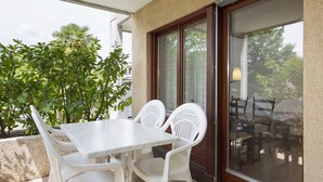 A patio with a white table and chairs, a glass door leading to an indoor area, and a view of greenery outside. - Resort al Centro by Interhome (Breganzona)