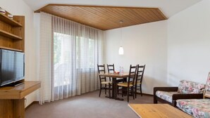 A cozy room with a wooden ceiling, a television on a wooden shelf, a dining table with chairs, a sofa with floral upholstery, and a window with sheer curtains. - Resort al Centro by Interhome (Breganzona)