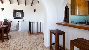 A modern kitchen with white walls, wooden beams, and a rustic stone floor.