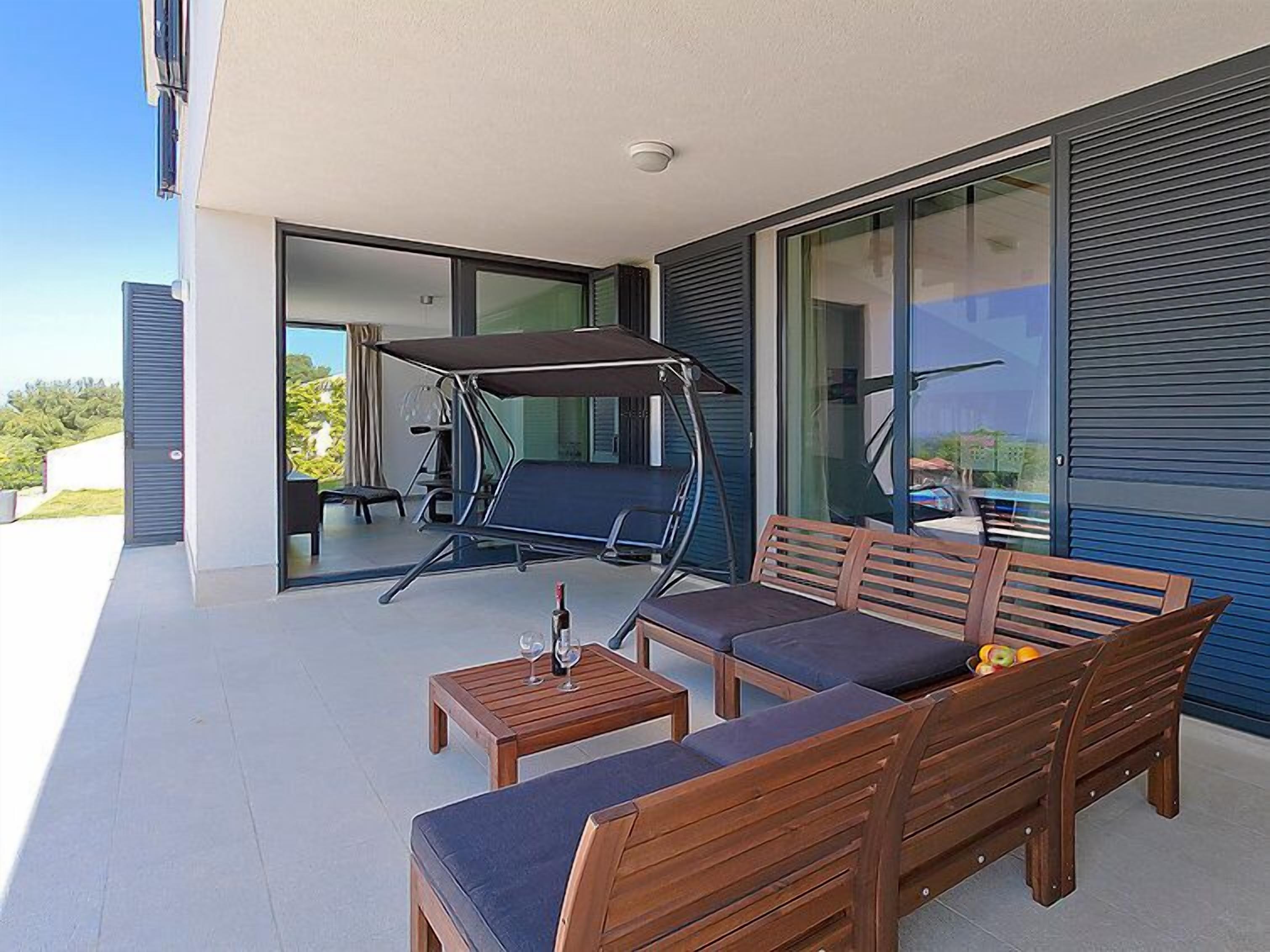 A balcony with a wooden sofa, a swing, and a table with glasses.