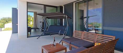 A balcony with a wooden sofa, a swing, and a table with glasses.