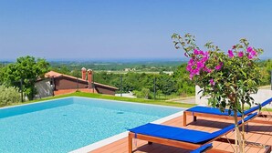 Área da piscina com espreguiçadeiras e vista para a paisagem.