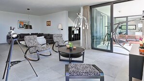 Uma sala de estar moderna com sofá, duas poltronas estampadas, uma mesa de centro, um telescópio e uma grande porta de vidro que dá para uma varanda.