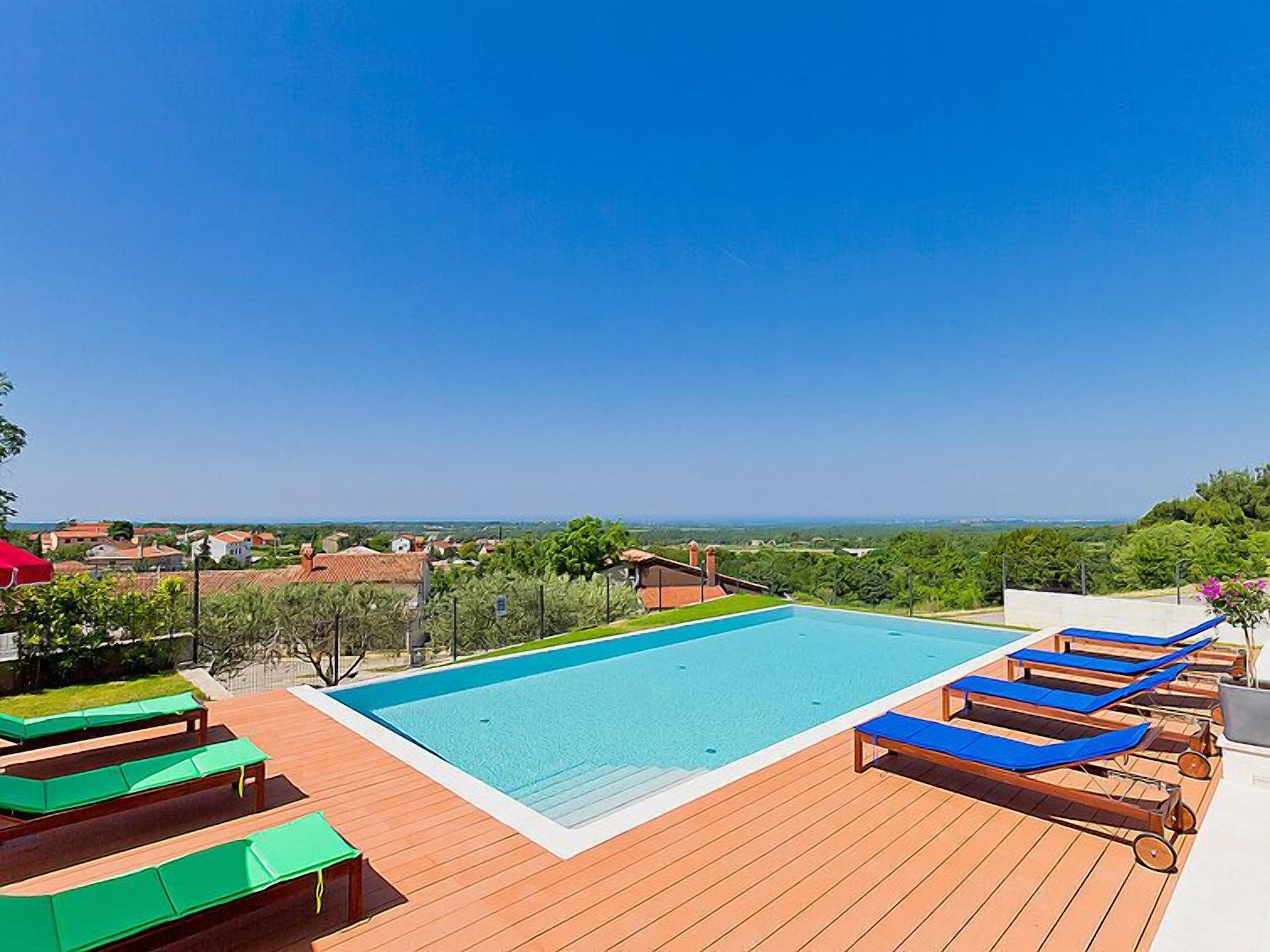 Un espace piscine doté d’une terrasse en bois, de chaises longues et offrant une vue sur le paysage.