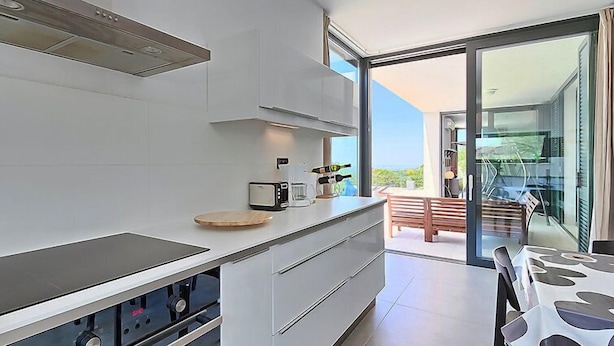 Cozinha moderna com uma ilha grande, forno embutido e área de refeições com mesa e cadeiras.