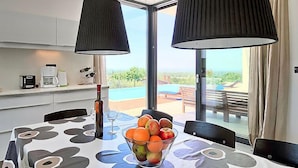 Uma área de refeições com uma mesa posta para dois, uma tigela de frutas e uma cafeteira no balcão.