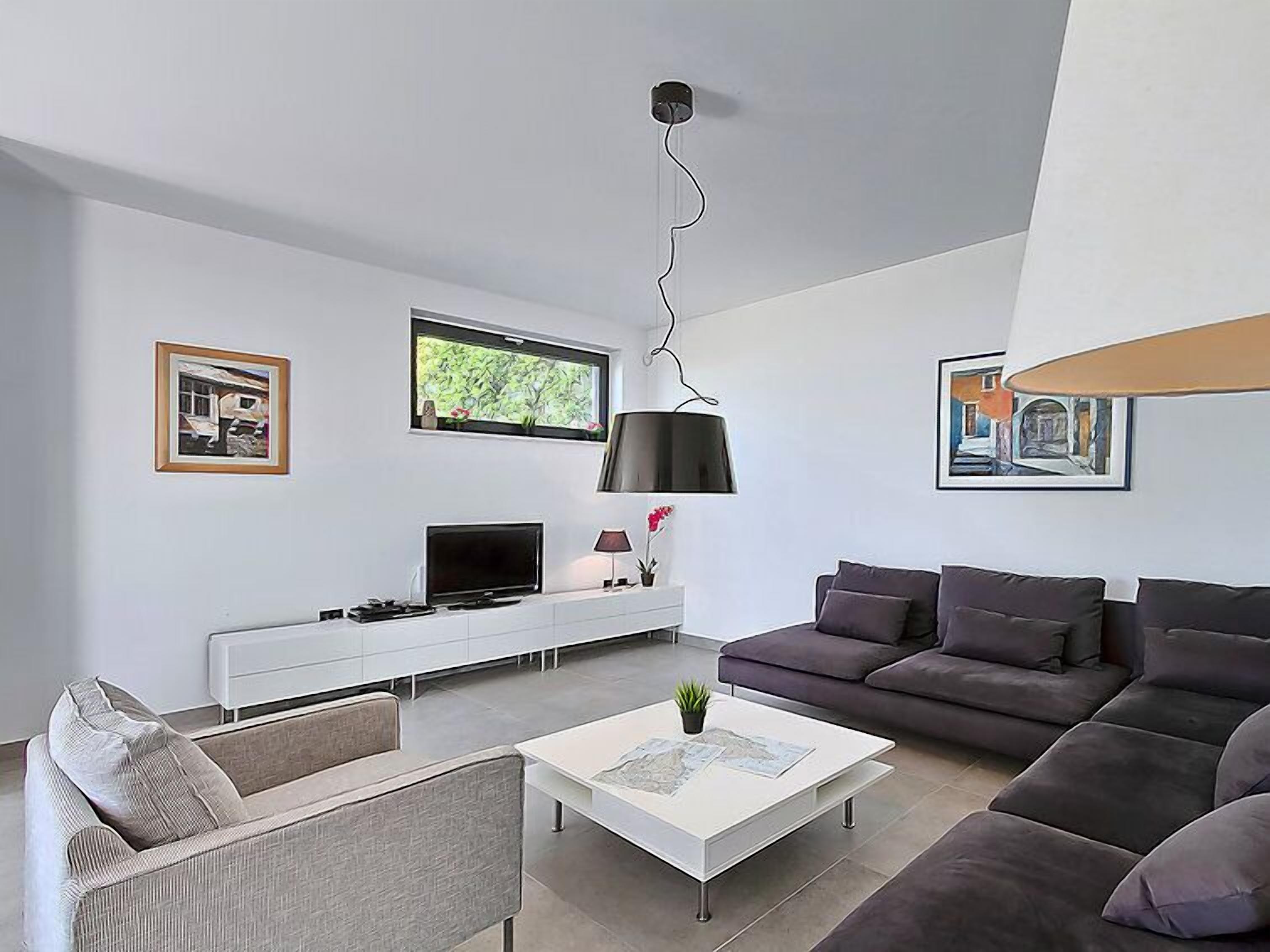 Un salon moderne avec un canapé, une table basse, un téléviseur et des œuvres d’art accrochées aux murs.