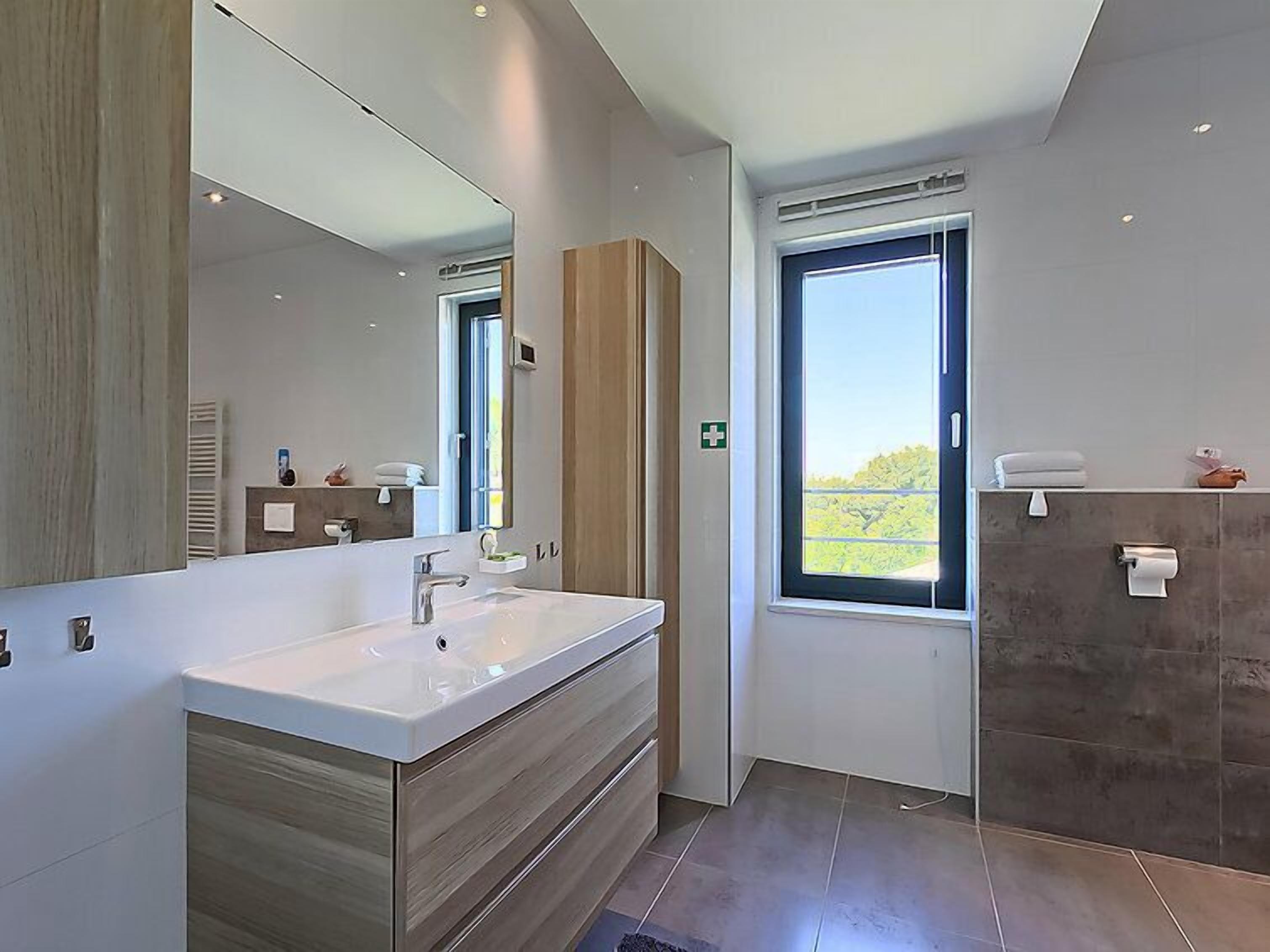 Une salle de bain moderne dotée d’un grand miroir, d’un double vasque et d’une fenêtre offrant une vue sur l’extérieur.