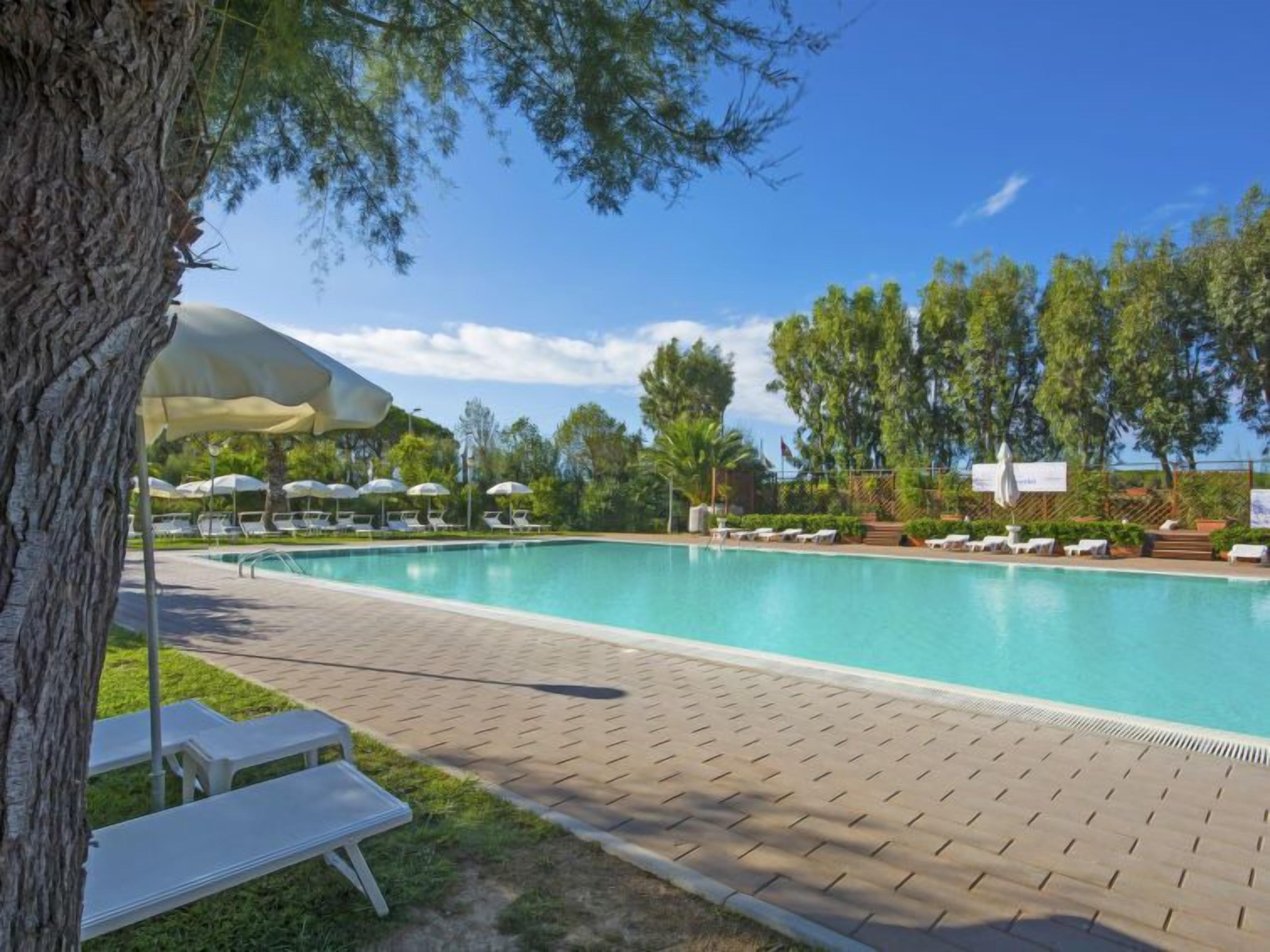 A rectangular swimming pool with a tiled deck, surrounded by lounge chairs and umbrellas.