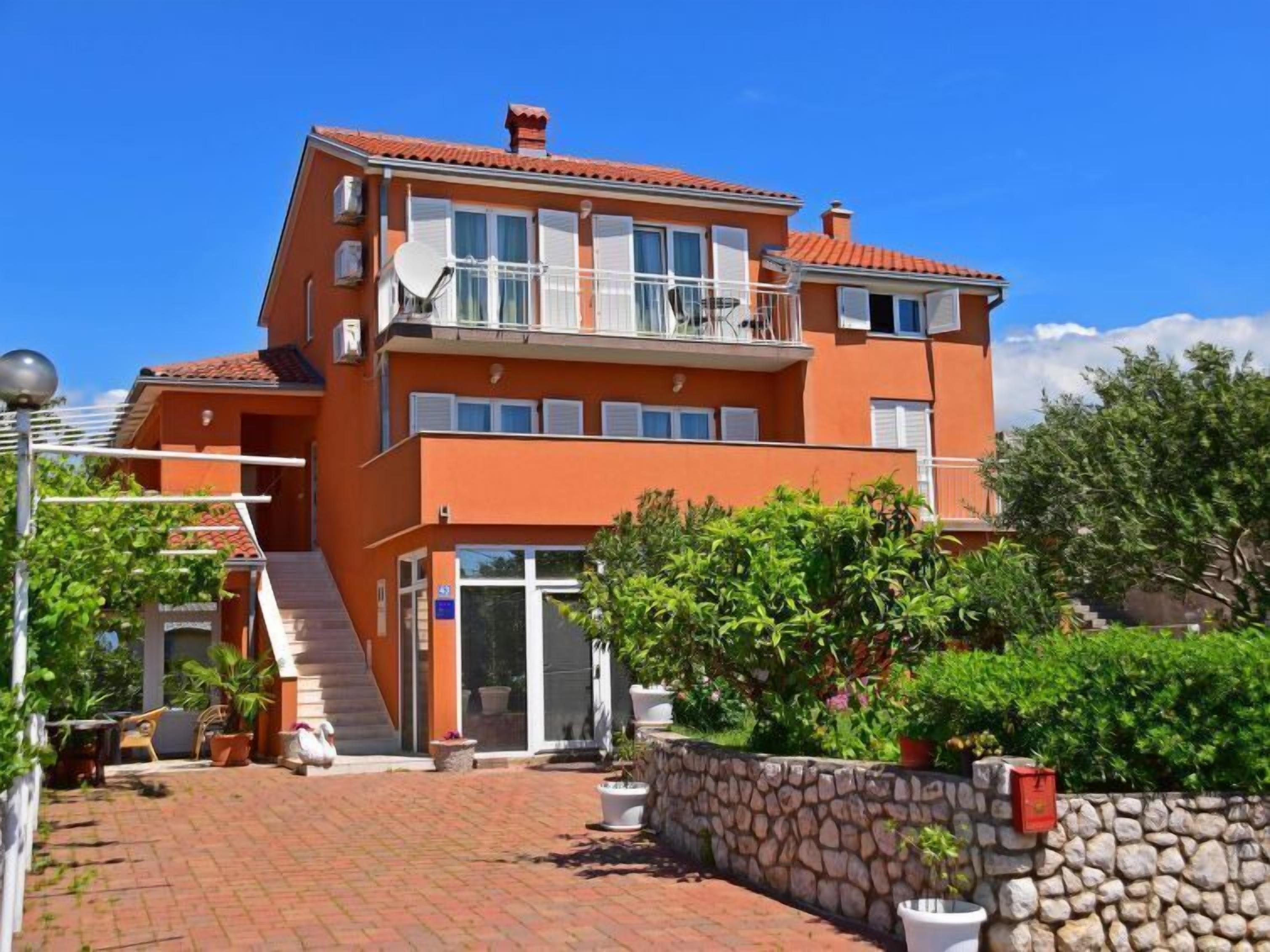 Ein zweistöckiges Gebäude mit einem Balkon im oberen Geschoss, einer Steinmauer und Blumentöpfen.