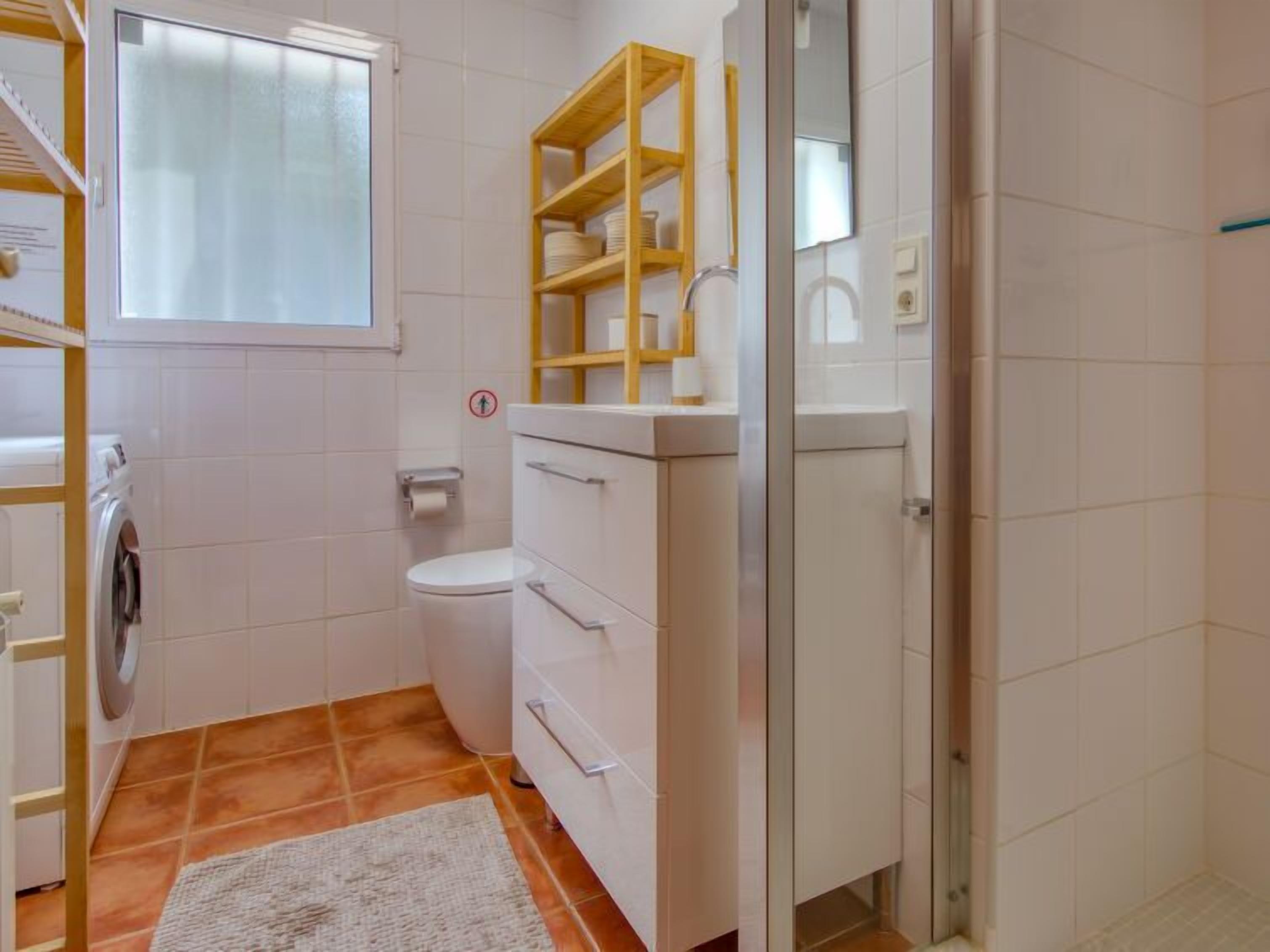 Une petite salle de bain comprenant des toilettes, un lave-linge et une douche à parois de verre.