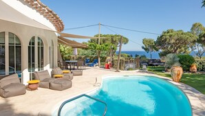 Ein Poolbereich mit geschwungener Kante, Gartenmöbeln und Blick auf das Meer.