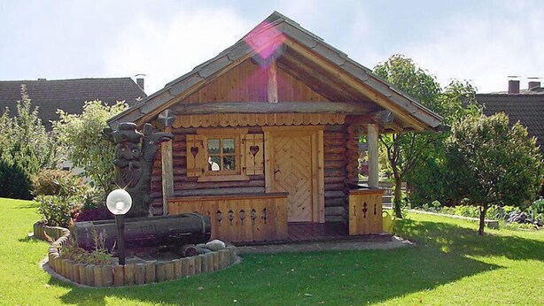 A log cabin with a chimney, a small porch, and a decorative lion statue. - Schnitzer by Interhome (Seeboden)