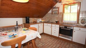 A kitchen with wooden cabinets, a tiled floor, a dining table with chairs, and a hanging light fixture. - Schnitzer by Interhome (Seeboden)