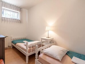 A small, single-bed room with a wooden bed, a bedside table with a lamp, and a window with blinds. - Apartment Kate by Interhome (Opatija/Mihelici)