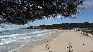 A beach with a clear view of the ocean, a sandy shore, and a distant hill with buildings. - Vistamar by Interhome (Torredembarra)