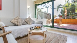 A modern living room with a sofa, a round wooden table with a tray of snacks, and a large window with a view of greenery outside. - Vistamar by Interhome (Torredembarra)