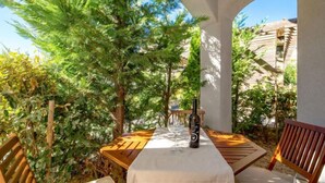 An outdoor patio with a table and chairs, surrounded by greenery and a clear view of the sky.