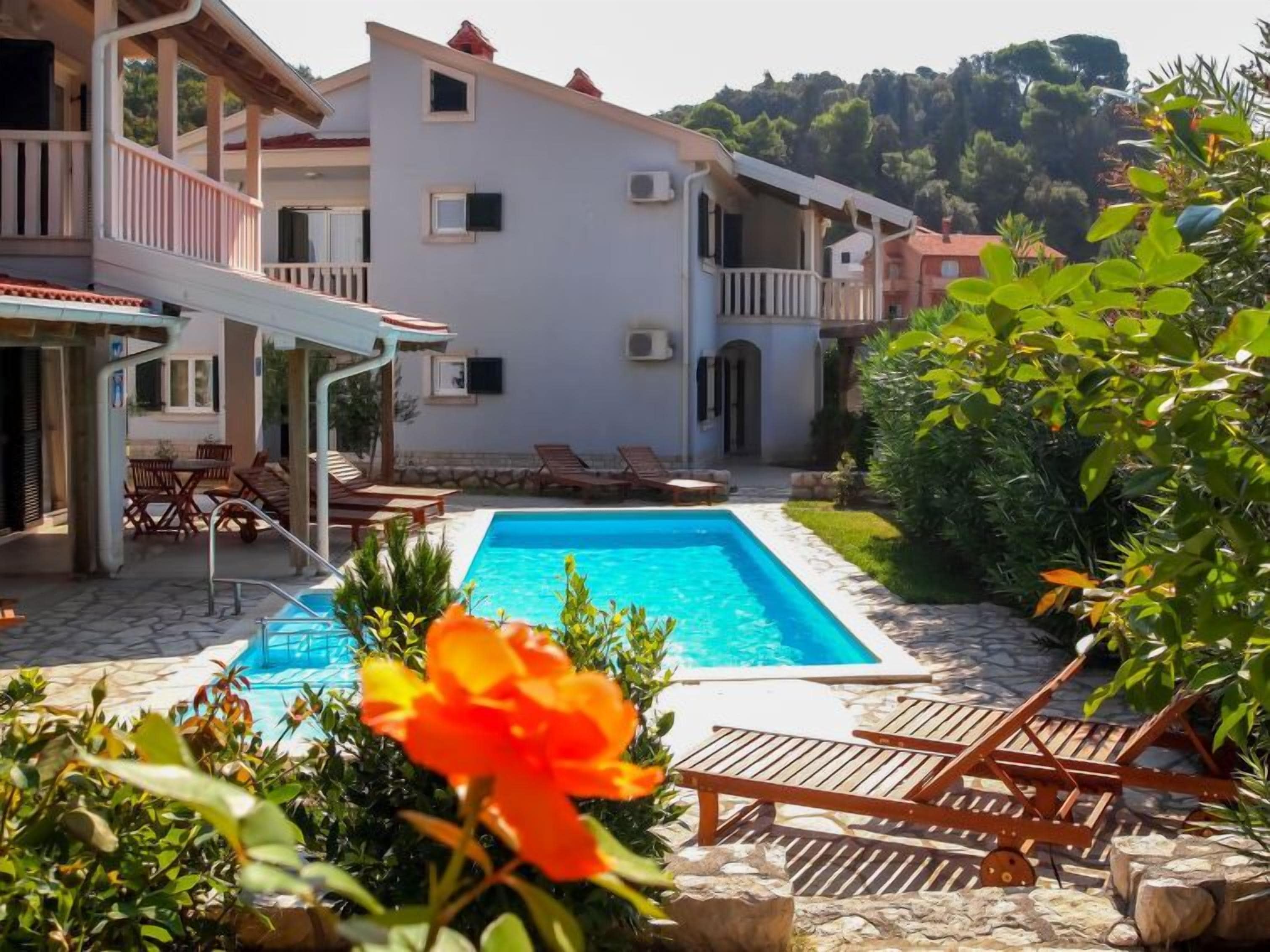 Zona de piscina con sillones de descanso y un edificio blanco con balcones.