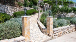 Un chemin de pierres mène à une propriété située sur une colline, qui est entourée d’un mur de pierres et agrémentée d’un lampadaire.