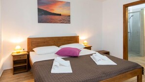 Une chambre d’hôtel avec un lit, une table de chevet, une lampe de chevet, un tableau représentant un coucher de soleil et une porte en verre pour la douche.