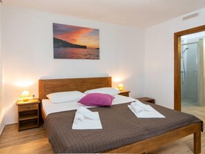 Ein Hotelzimmer mit einem Bett, einem Nachttisch, einem Beistelltisch, einem Abendhimmel-Gemälde und einer Duschkabine aus Glas.