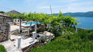 Un bâtiment en pierre doté d’une piscine, entouré d’une végétation luxuriante et offrant une vue sur la mer.