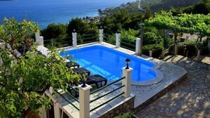 Une piscine bordée de pierres, entourée de verdure et offrant une vue sur la mer et les montagnes.