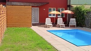 Een achtertuin met een zwembad, twee ligstoelen en twee parasols.