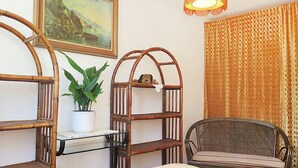 Een kamer met een bed, een stoel, een plank met een plant, een schilderij aan de muur en een gordijn met een patroon.