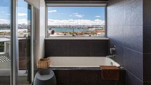 A modern bathroom with a large bathtub, a view of a cityscape and water body, and a balcony with a glass door. - Villa Vogue by Interhome (Ferragudo)