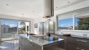 A modern kitchen with a large island, stainless steel appliances, and a view of the city through large windows. - Villa Vogue by Interhome (Ferragudo)