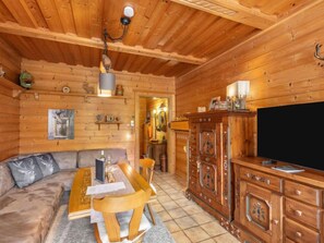 Ein gemütliches Blockhaus-Interieur mit Holzbalkendecke, einer Couch, einem Esstisch, einem Schrank und einem Fernseher.