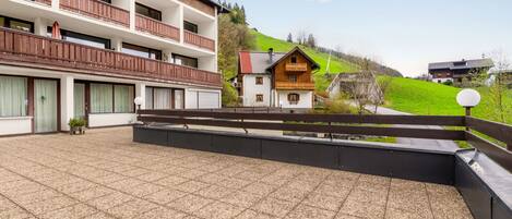 A hotel with a terrace, a wooden balcony, and a view of a green hill.